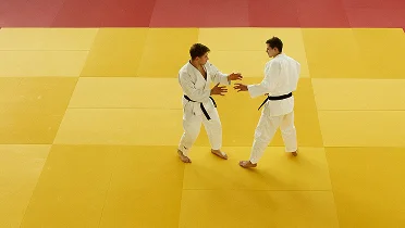 Two judo athletes practicing stance and grip techniques on a yellow tatami mat, focusing on balance, positioning and controlled movement in training